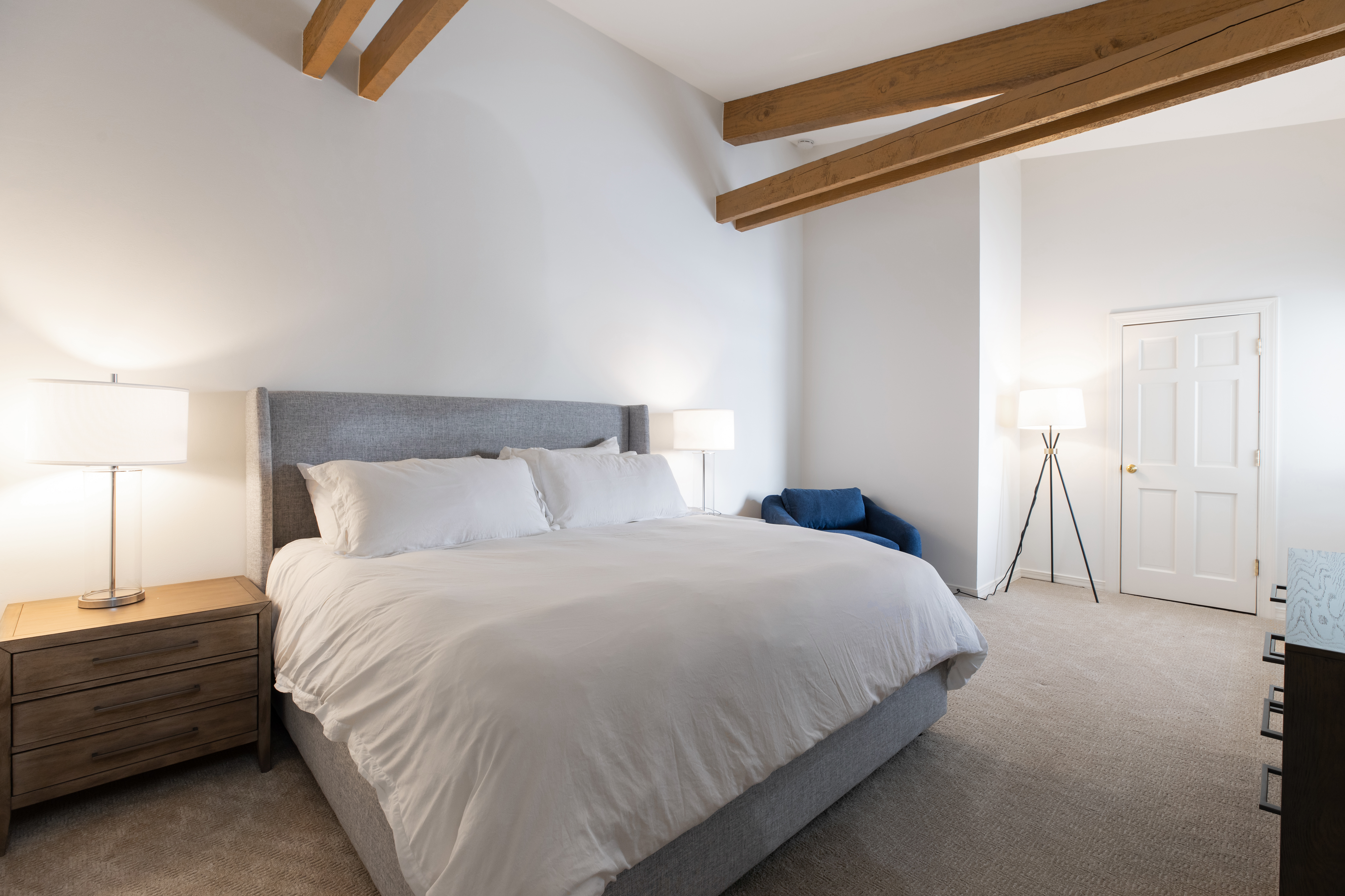 A wide view of a guest room with a bed, nightstand, and lamp.