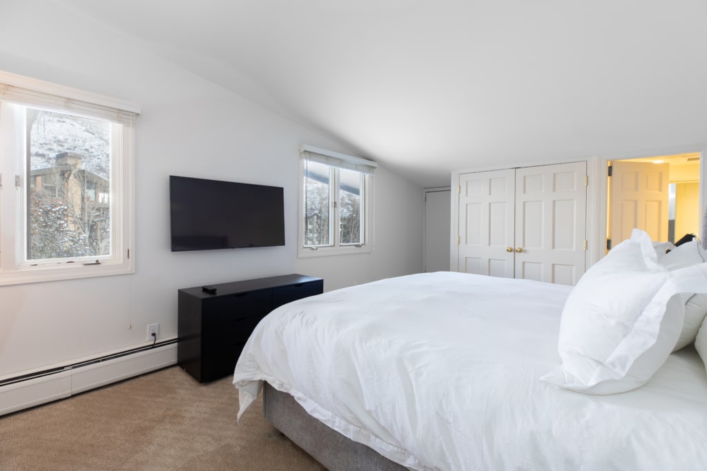 A guest room with a large bed, TV, and window