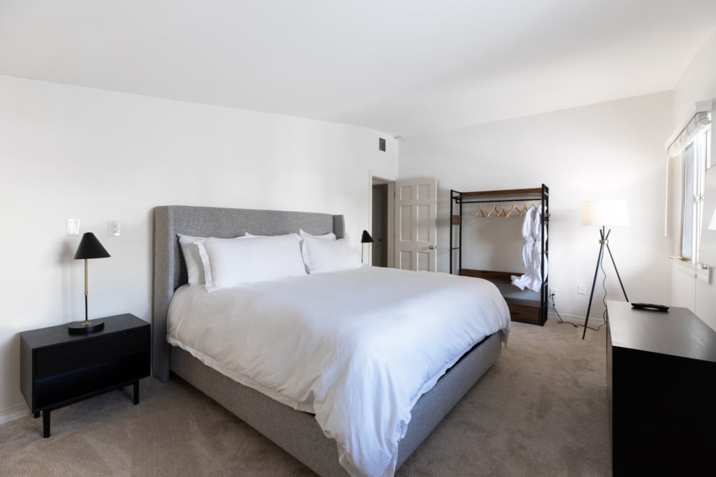 A wide view of a hotel room with a large bed, nightstand, dresser, and standing rack.