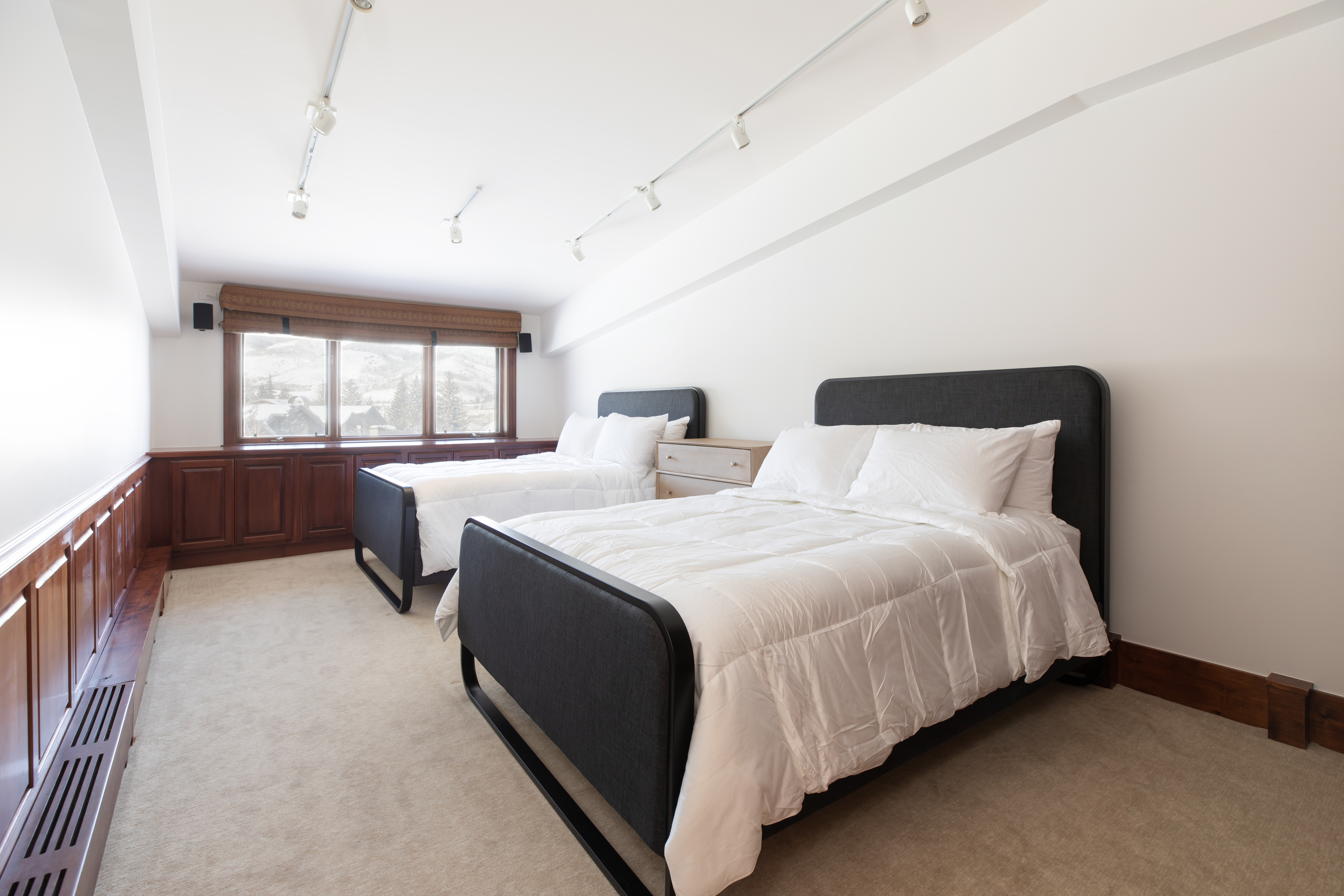 A hotel room with two beds, a window, and track lighting.