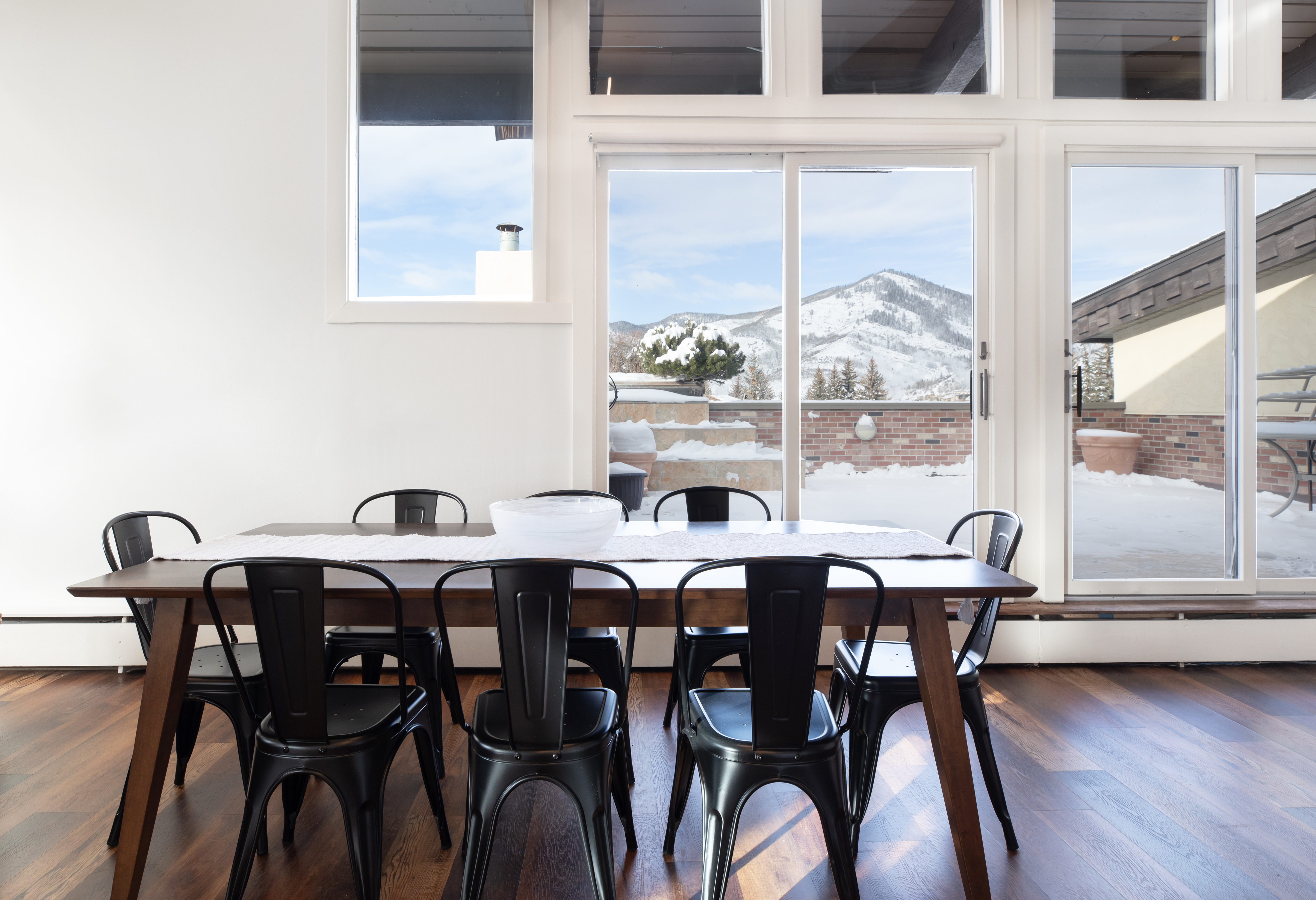 A dining area with a table and chairs in front of a large window showing a mountain view.