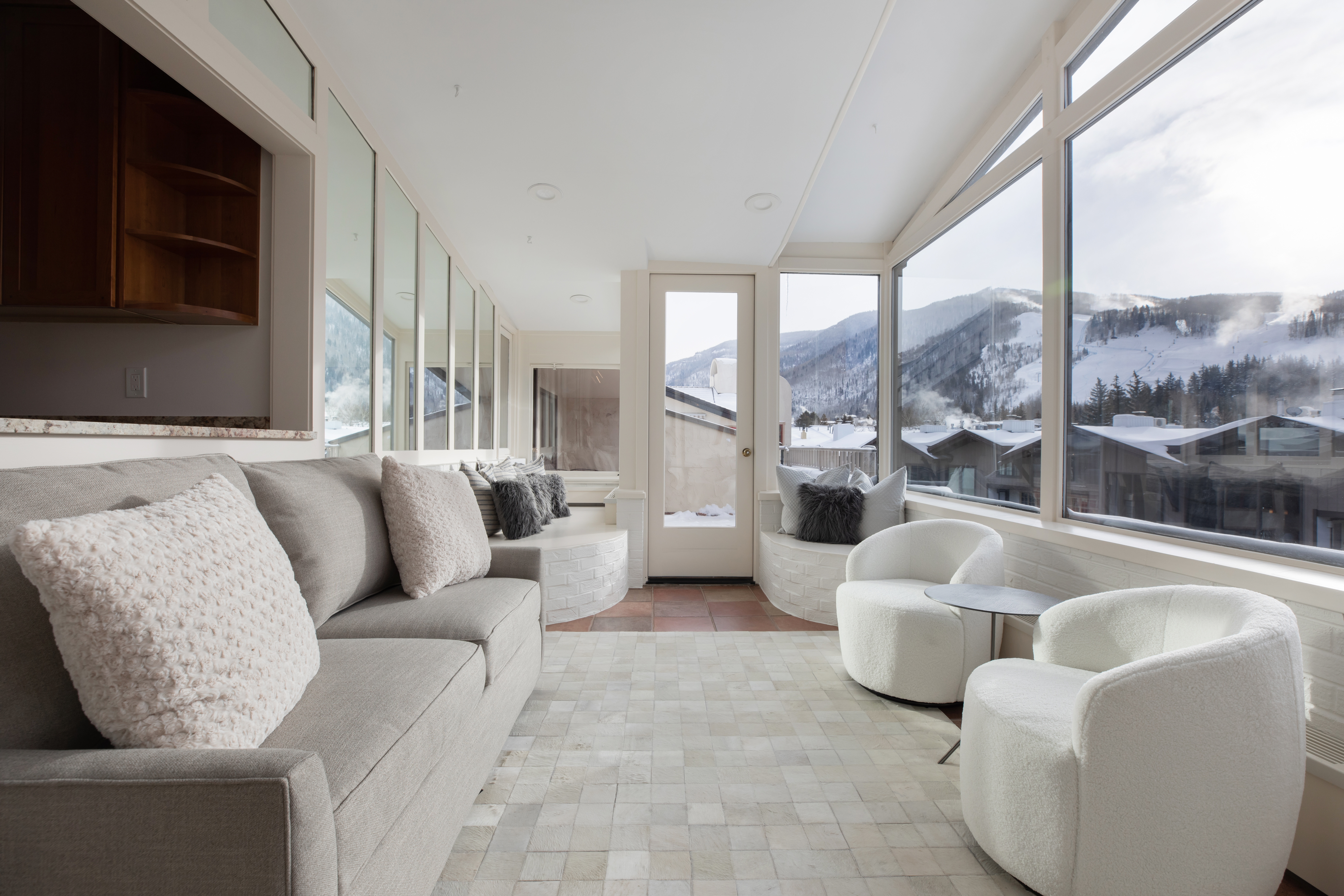 A modern lobby with a sofa, armchairs, and a coffee table in front of large windows showing a mountain view.
